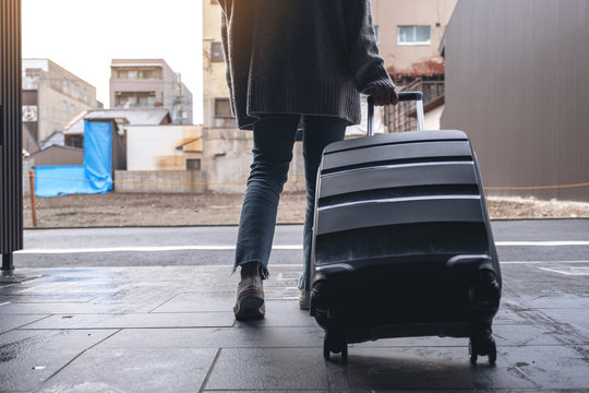 Closeup image of a woman walking while traveling and dragging a black baggage in the outdoors