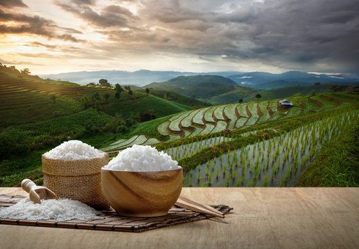 Jasmine rice and steamed rice in wooden bowl with the chopsticks on the wooden table with the plantation rice at sunset