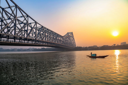 Historic Howrah bridge at Kolkata with view of fishing boat on river Ganges at sunrise 