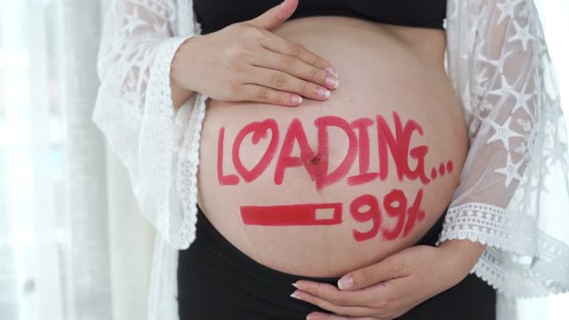 panning shot of pregnant woman with loading 99% concept painted on her belly
