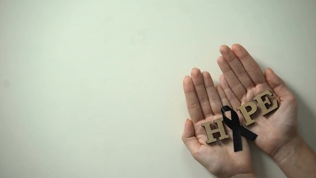Woman hands showing black ribbon to camera, melanoma awareness, skin cancer