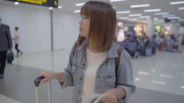 Slow motion - Happy Asian woman using trolley or cart with many luggage walking in terminal hall while going to boarding flight at the departure gate in international airport.