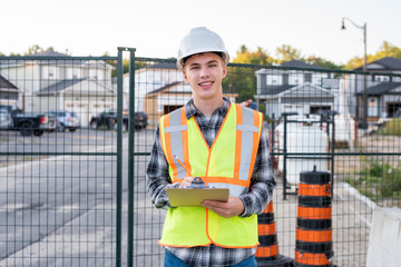 Happy young construction worker wearing safety gear and holding a clipboard.