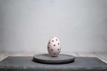 Painted Easter egg on a concrete stand on a light background.