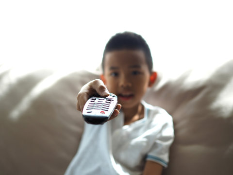 Cute Asian boy holding a television remote controller. (Selected focus)