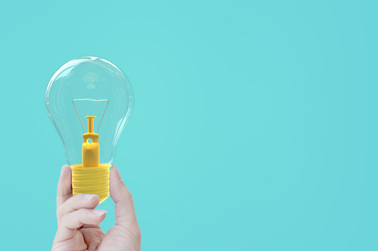 Hand holding light bulb yellow pastel color on blue background