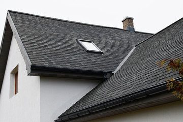 Part of white house with new wooden eaves, plastic rain gutter, window and chimney in grey shingles...