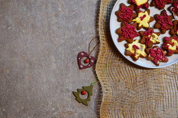 Homemade decorated gingerbread in white plate on gray grunge table with linen tablecloth top view decorative xmas bells on table. Merry christmas and happy new year concept.