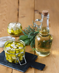 Marinated feta in a glass jar, spices and olive oil on a wooden background