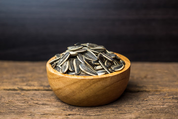 sunflower seeds group with a wooden cup on wood background. The name of science : Helianthus annuus