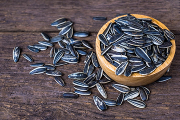 sunflower seeds group with a wooden cup top view on wood background. The name of science : Helianthus annuus.