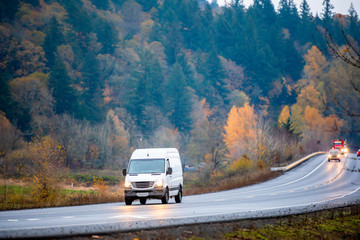 Compact cargo mini van for small business and local delivery driving in winding wet autumn road in...