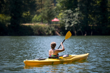 Elderly woman in bathing suit swims with paddle on kayak on lake surrounded by forest