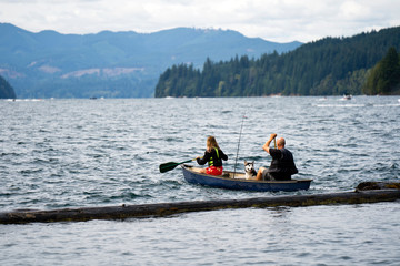 Fototapeta na wymiar Girl and man with husky dog on kayak with oars in their hands overcame log breakwater on Lake Merwin and go fishing