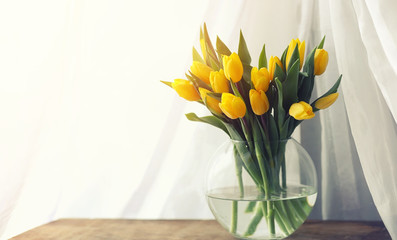 A bouquet of red tulips in a vase on the windowsill. A gift for a woman's day from red tulip flowers. Beautiful red flowers in a vase by window.