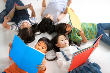 Kids reading book laying on the white floor ,head to head, in a circle group, preschool...