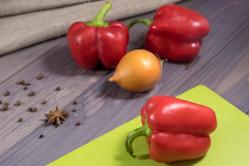 Three sweet red peppers with onion on the table. Process of cooking.