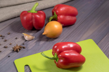 Three sweet red peppers with onion on the table. Process of cooking.