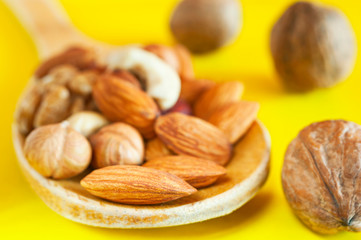 Almonds, Hazelnuts, Walnuts, Cashew Nuts in a Wooden Spoon, and Three Whole Walnuts Isolated on Yellow Background. Healthy Organic Snack, Breakfast, Food Ingredients.