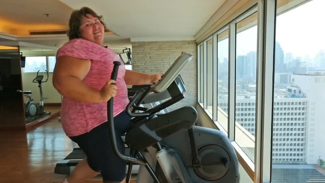 Overweight woman exercising on a cross-trainer machine in gym