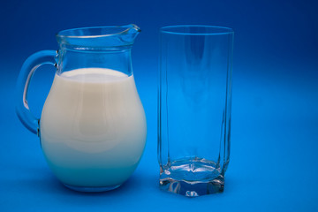 A jug of milk and empty glass on a blue background
