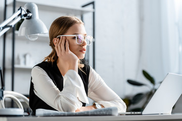 tired businesswoman in formal wear and glasses sitting at computer desk at workplace