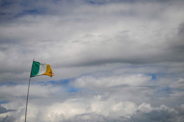 National flag of Ireland torn by strong wing, on flagstaff, cloudy sky in the background.
