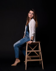 girl in the blue denim suit with a white pullover sitting on the wooden steps on black background