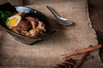 stewed eggs and pork in black bowl and spices place in front of and spoon stainless steel place backside on Sack  and wood background