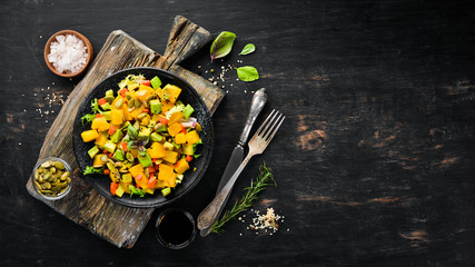 Salad of pumpkin, avocado and pumpkin seeds. On a black background. Top view. Free space for your text.