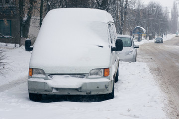 Car covered with fresh white snow in the city. Minibus under the snow. Sleet slush, ice covering on the roads, and southeastern