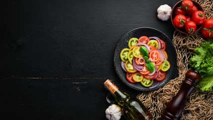 Salad of fresh tomatoes and onion in a black plate. On the old background. Top view. Free space for your text.