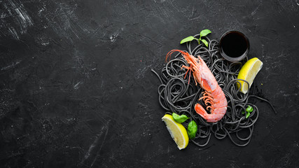 Black pasta with shrimp on a black stone background. Top view. Free space for your text.