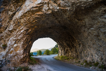 Road going through Hairpin turn rocky tunnel with mountain view and green trees and sunset