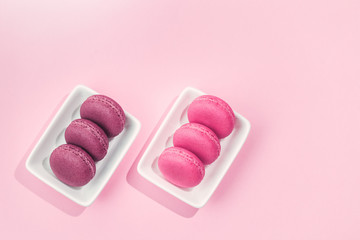 Several sweet tasty pink macaroons in white bowls on pink background with copy space closeup