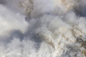 Close up of rough water. On the surface of the water a lot of foam and spray. Abstract background. Empty background. Stormy water. Sea, ocean, waterfall.