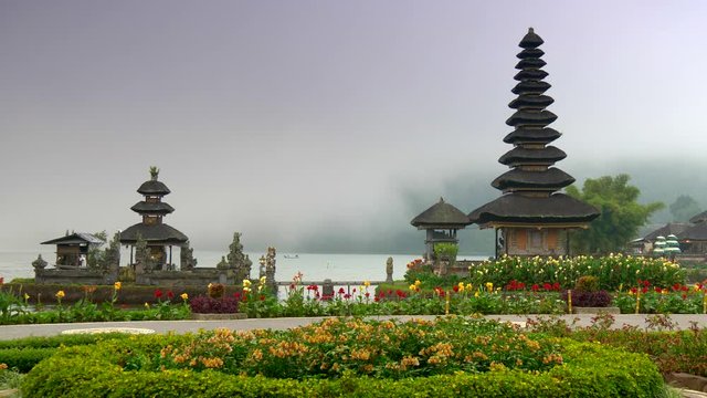 Bali, Indonesia. Pura Ulun Danu Bratan Temple surrounded by beautiful flowers with mist covered water in the background. Pura Bratan is a water temple of shaivism (worship Shiva). 4K