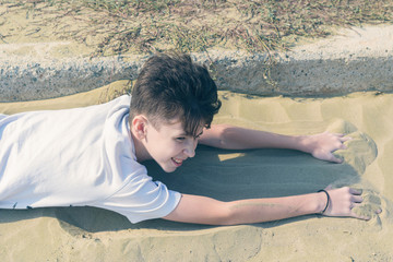 A boy in a T-shirt and shorts with sneakers lies on the sandy  beach