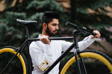 Fototapeta na wymiar Young hipster indian boy in glasses holding green bicycle at sunny summer street