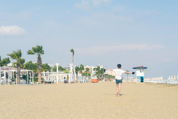 A boy in a T-shirt with sneakers on the sandy Mackenzie beach in Larnaca. Cyprus island