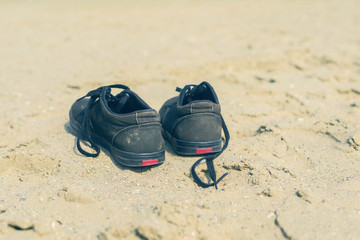 Fototapeta premium Black sneakers on the sandy beach on the sea background. Summer and travel concept