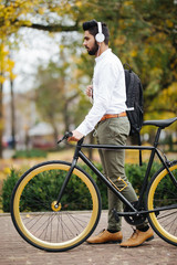 Fototapeta premium Indian Businessman listening to music while walking to office with his bike. Man enjoying his commute to office walking with his bicycle