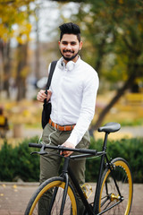 Confident young indian businessman with bag walking with bicycle on the street in town