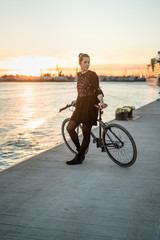 Young woman with her bicycle in harbour while sunset