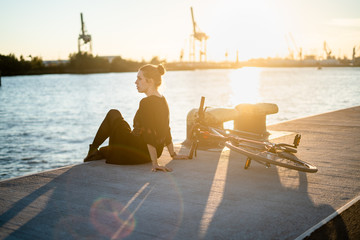 Young woman with her bicycle in harbour while sunset