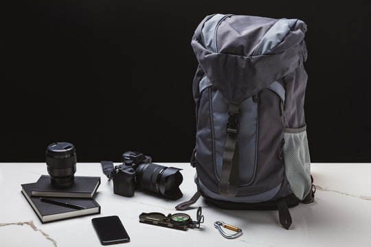 backpack, smartphone, compass, notebooks and photo camera with lens on black