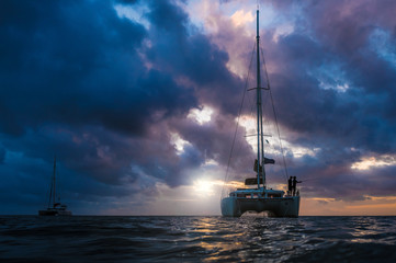 The dark silhouette of catamarans on open sea with dramatic clouds during sunset. The fisherman fishing on bow