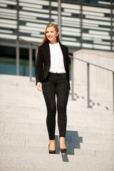 Obraz premium Young business woman walks down stairs near office building