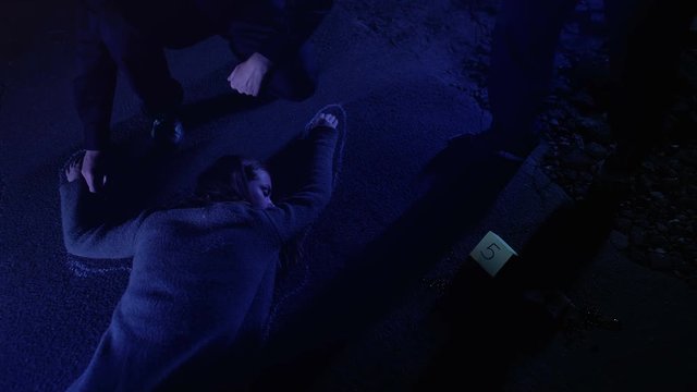 Cop fixing position of corpse with chalk, college making photos of evidence