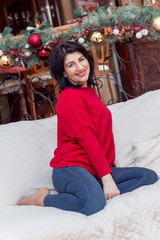 Beautiful woman in her forties, in red blouse smiling, sitting on the couch, christmassy atmosphere